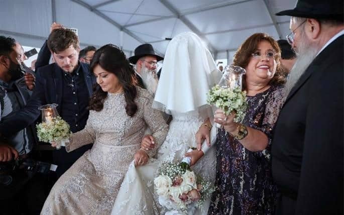 La novia, escoltada por su madre y su suegra, rodea al rabino Levi Duchman bajo la jupá, el dosel nupcial. Crédito: EAU judío/Christopher Pike.