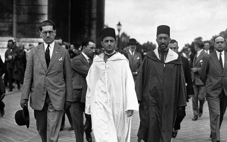 Mohammed V de Marruecos, vestido con túnica blanca, camina junto al Gran Visir del país, Si Mohammed El Mokri, después de que este depositara una corona de flores en la Tumba del Soldado Desconocido en el Arco del Triunfo durante una visita a París, Francia, alrededor del 4 de julio de 1930. (Foto AP)